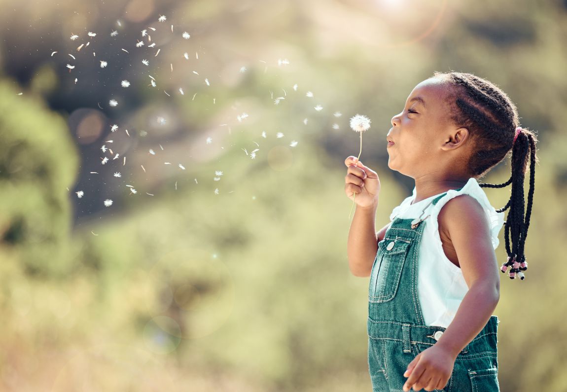 child blowing on a dandelion