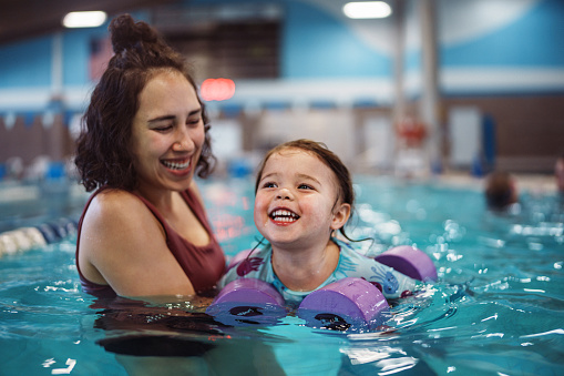 Smiling girl learning how to swim with her mom.