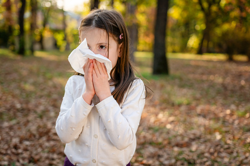 Young girl blowing her nose outside.