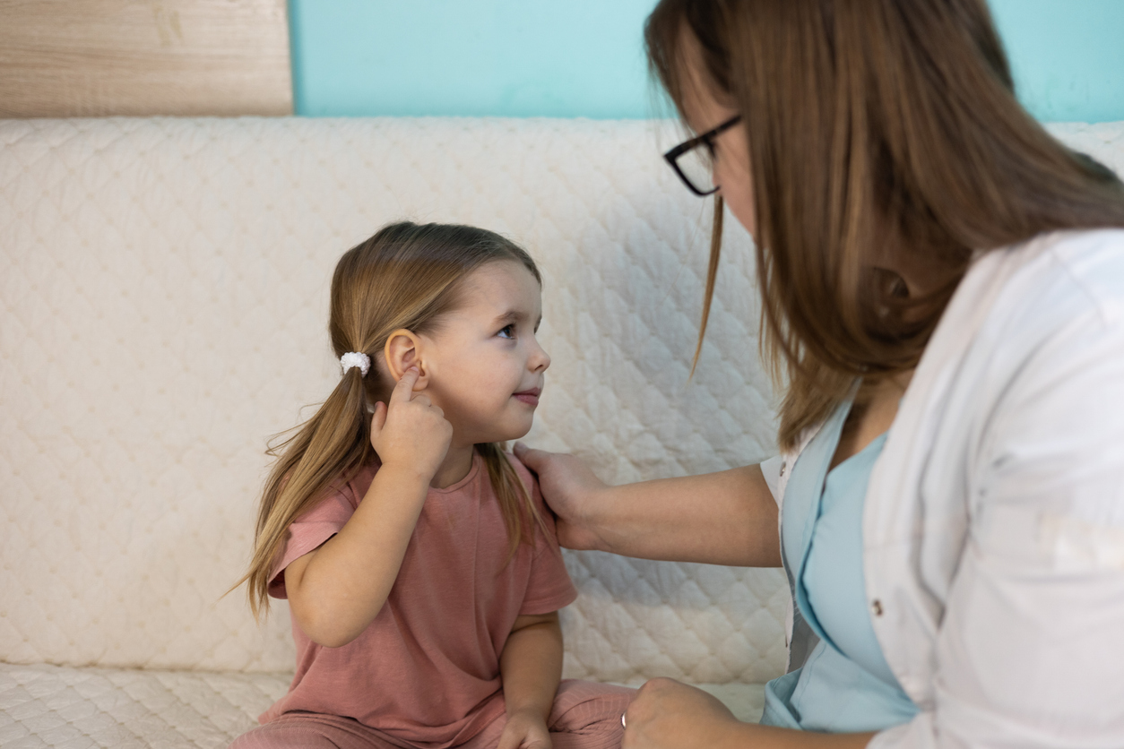 Young girl points to her ear to tell her doctor where it hurts.