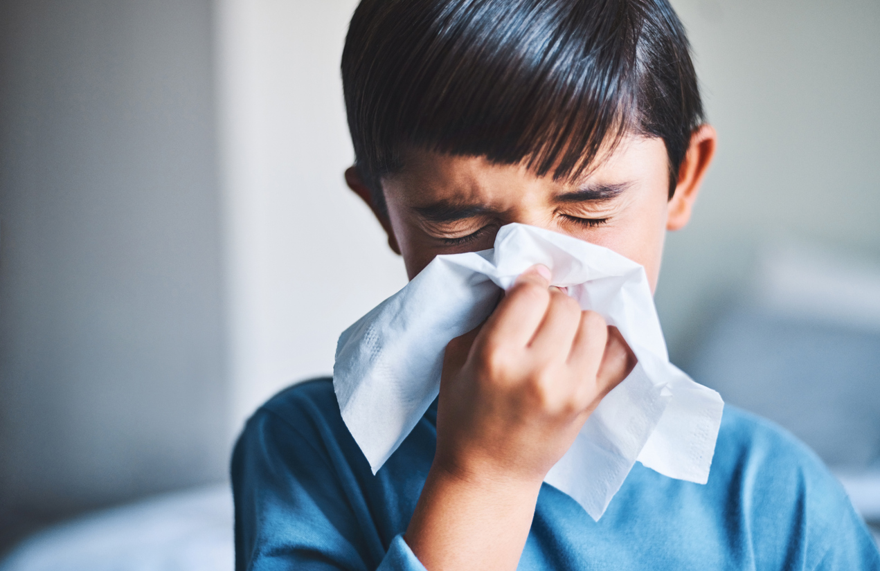 Cropped shot of a little boy blowing his nose while standing in his home