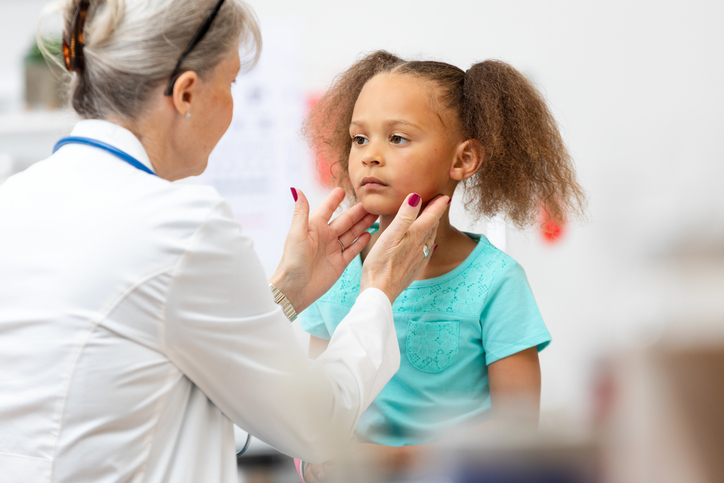 Doctor's hands gently feel a young girl's neck during a pediatric examination.  Indoor clinic setting.